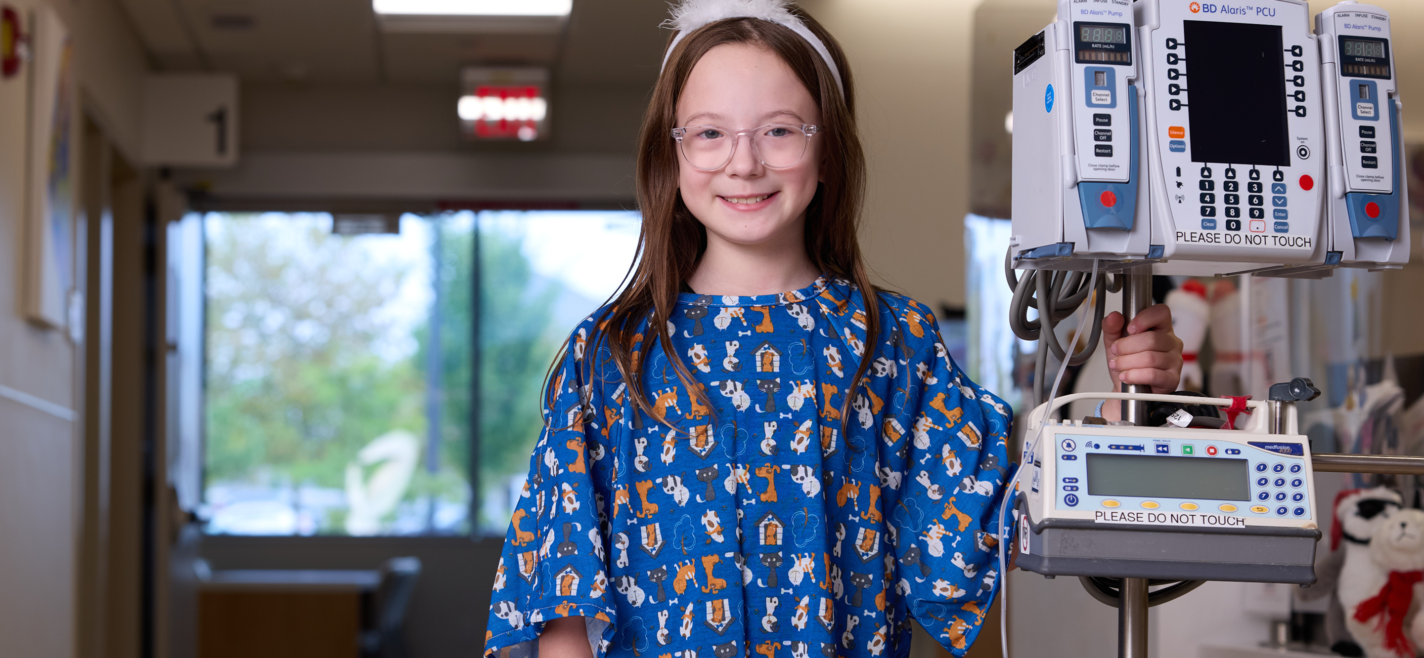 Children's National patient, Mackenzie, wearing a hospital gown and standing next to monitoring equipment.