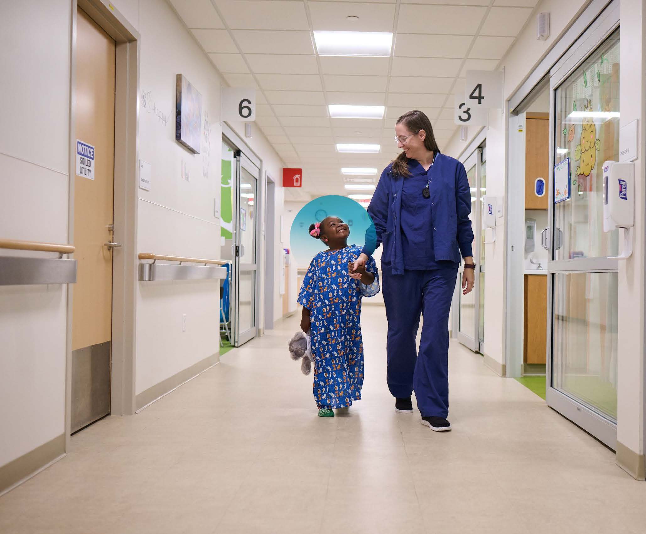 Provider and a young patient smile at one another as they walk down a hospital hallway
