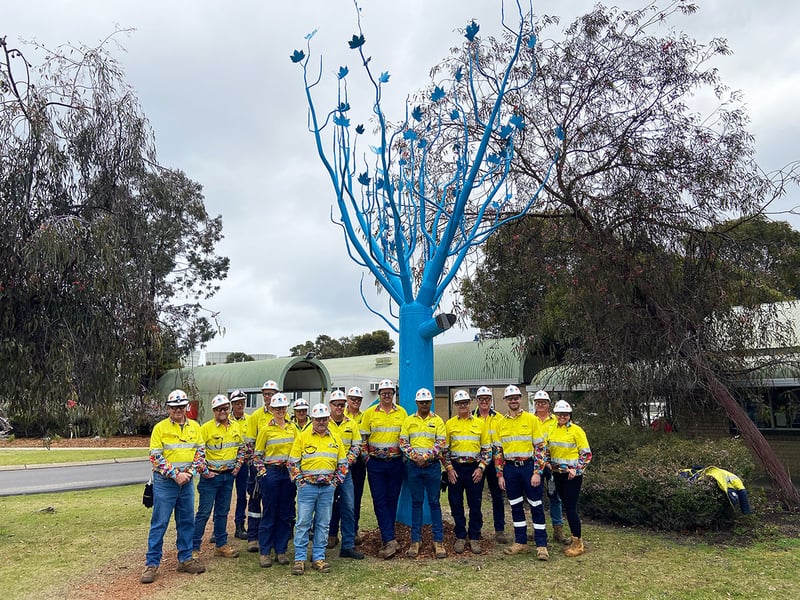 A group of people in yellow PPE standing in front of a blue artificial tree
