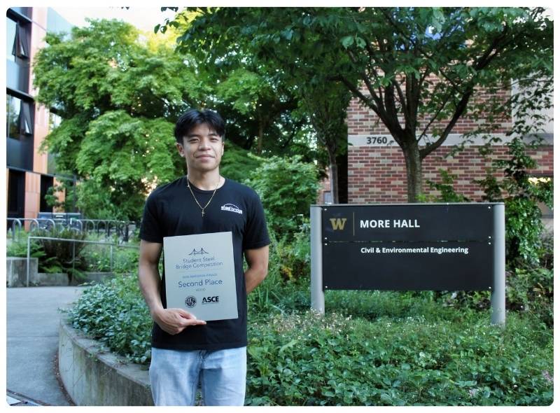 Étudiant universitaire masculin tenant un prix de deuxième place du concours étudiant de ponts en acier alors qu’il se tient devant le bâtiment de génie civil et environnemental de l’Université de Washington