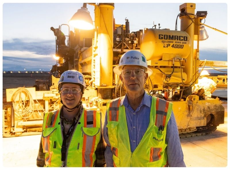 A man and a women in Pulice PPE standing in front of a paving machine