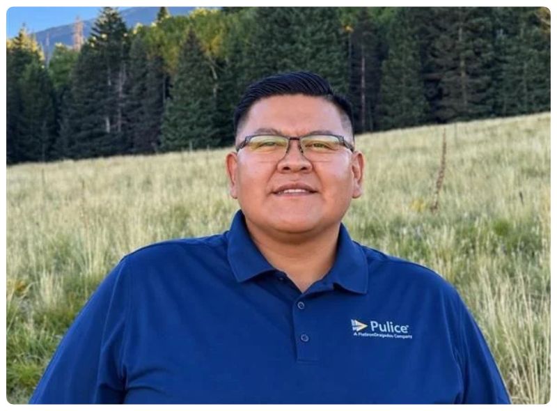 Man standing in a green field wearing a blue polo with the Pulice logo