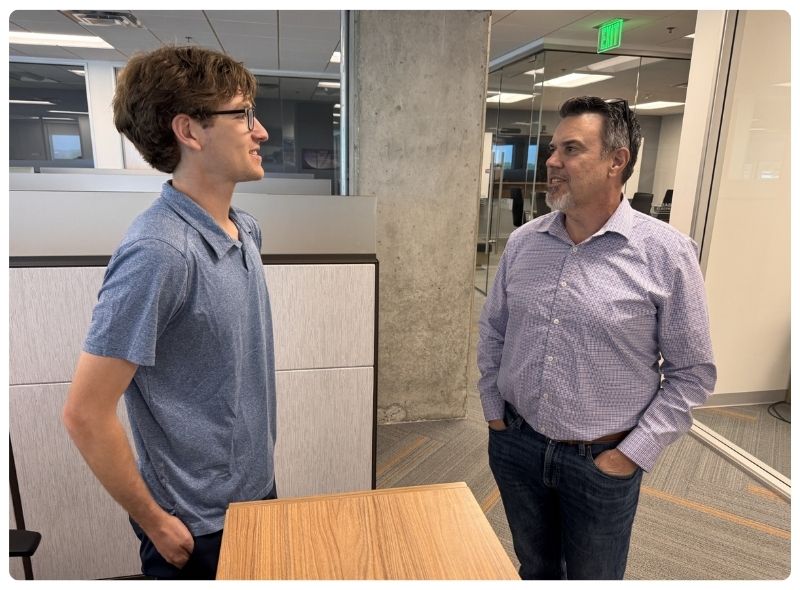 Two men are standing and talking in an office setting. 
