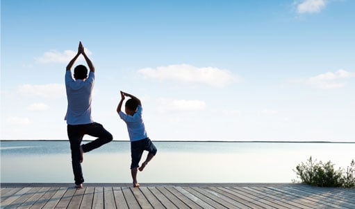 Father and son doing yoga by the lake