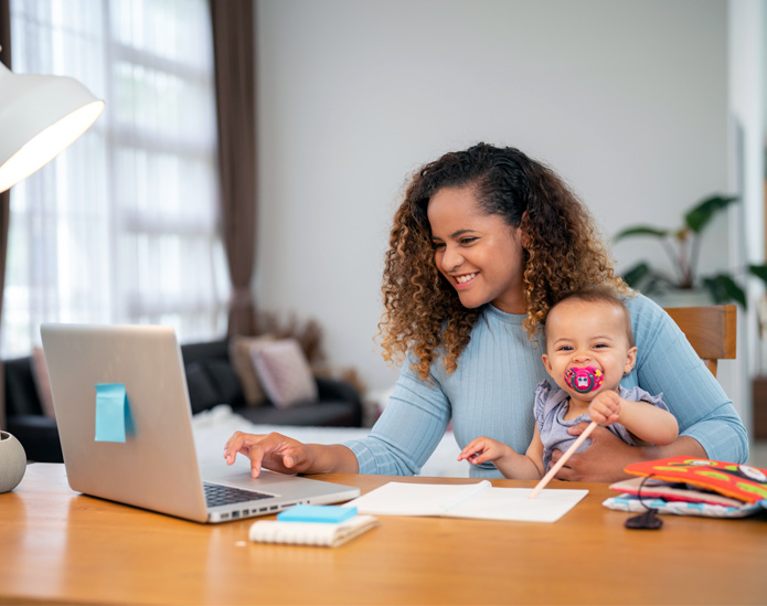 Mom holding baby while working on laptop