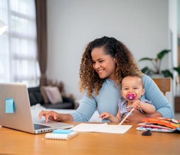 Mom holding baby while working on laptop