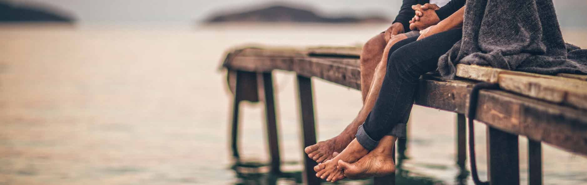 Shoeless couple sitting on a dock at sunset