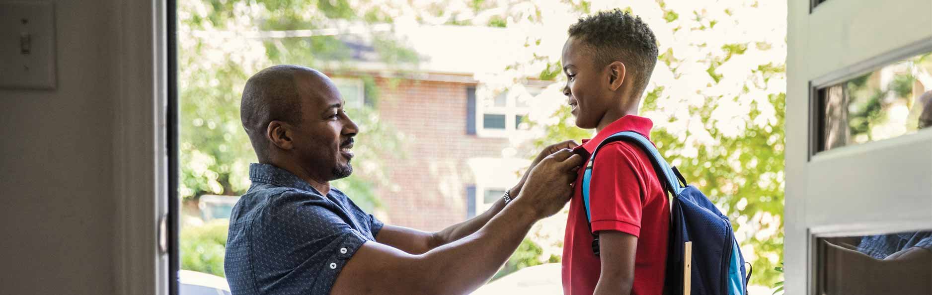 Father getting son ready for school on the front porch