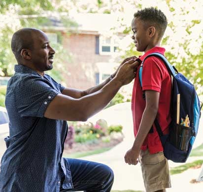 Father getting son ready for school on the front porch