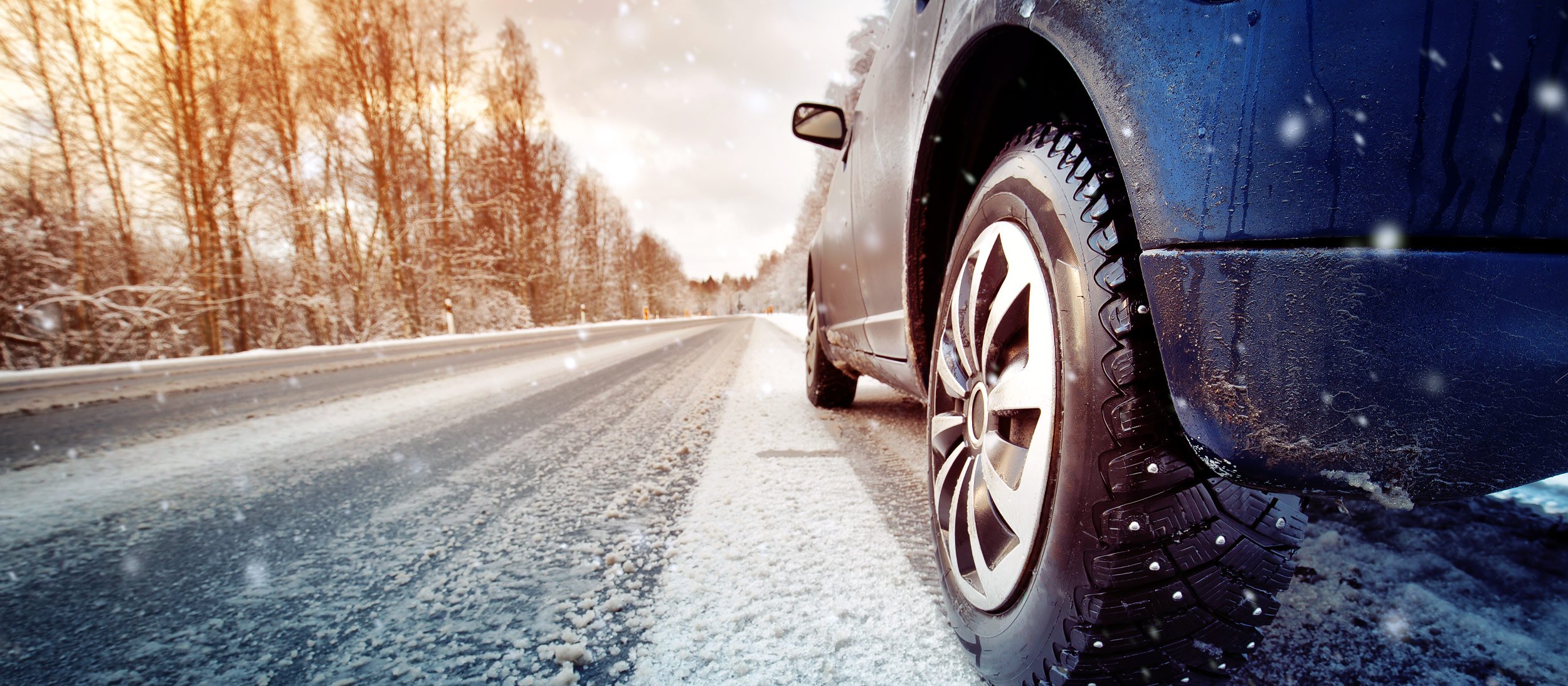 Road perspective of a car's tire driving on a snowy road