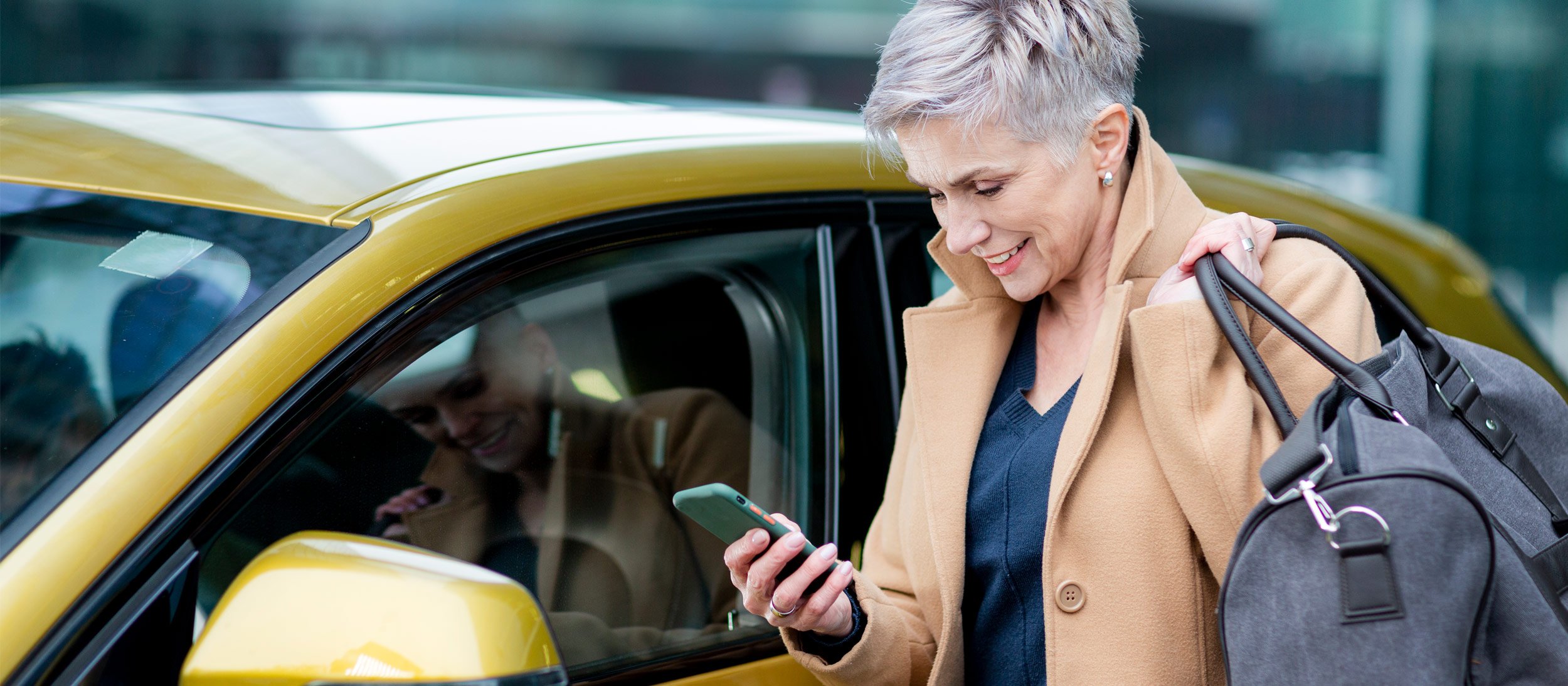 Woman looking at her cell phone next to a rental car
