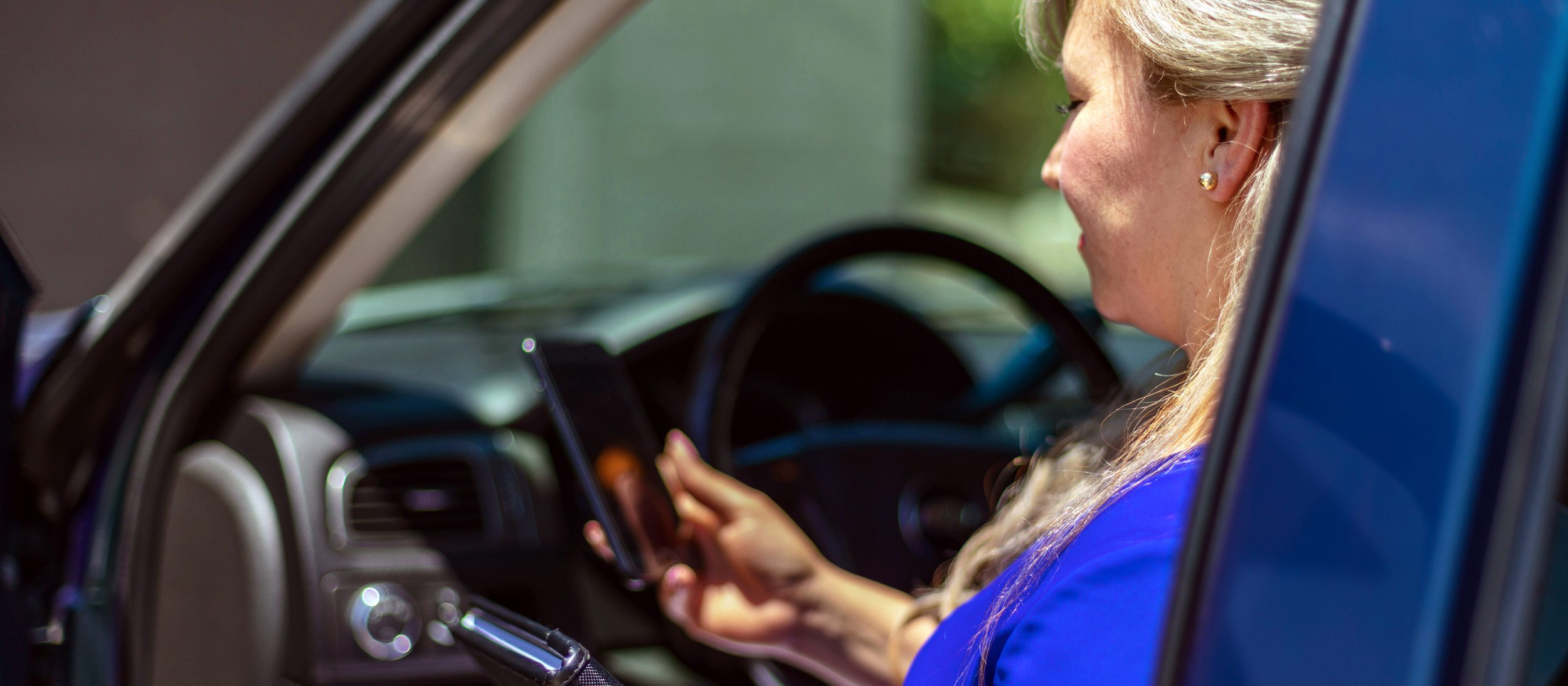 Woman looking at her phone sitting in the driver's seat of her vehicle