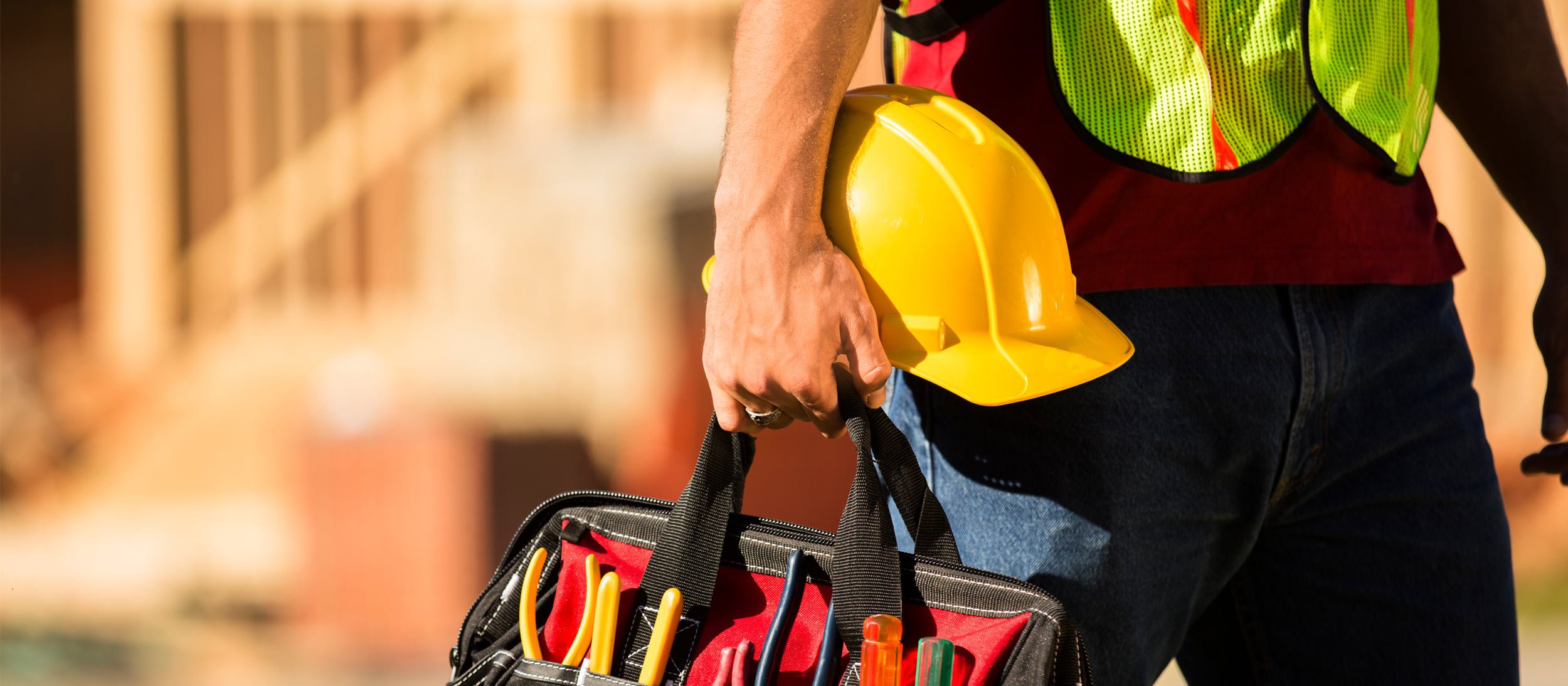 Construction worker walking with their hardhat and toolbag