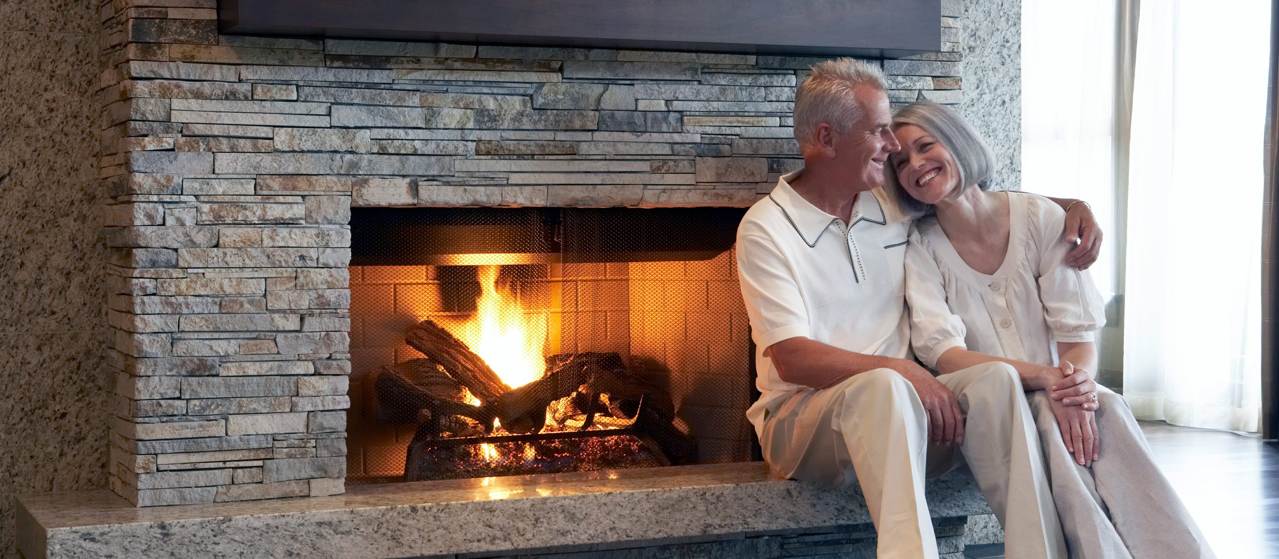 A couple sitting and smiling front of a fireplace