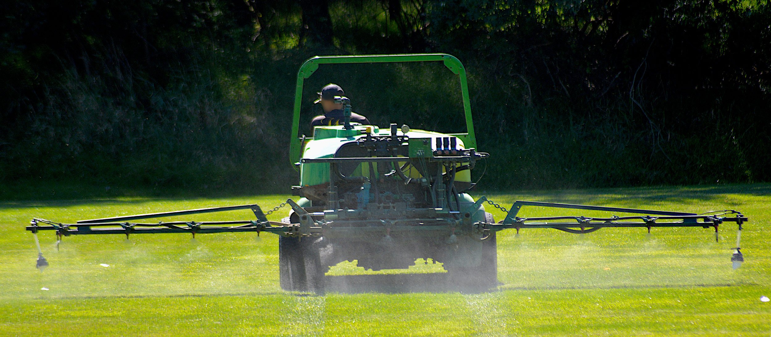 Employee watering the grass in a tractor with sprayers