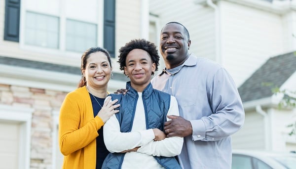 Parents stand behind their teenage son with their hands on his arms.