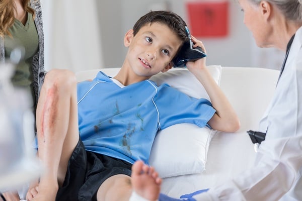 A boy with sports injury holds an ice pack to his head while a female caregiver looks on.