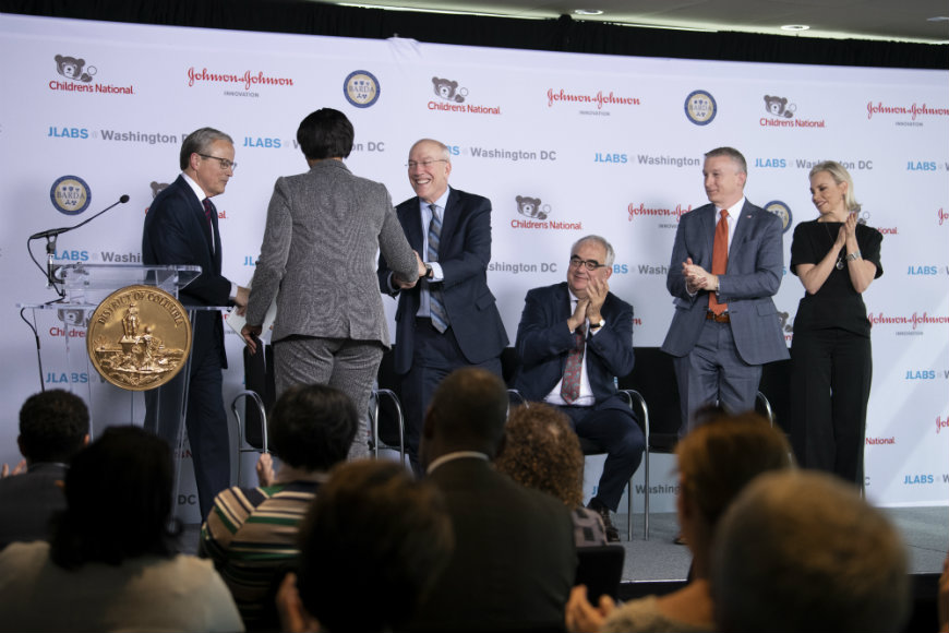 Speakers shake hands and applaud on the stage.