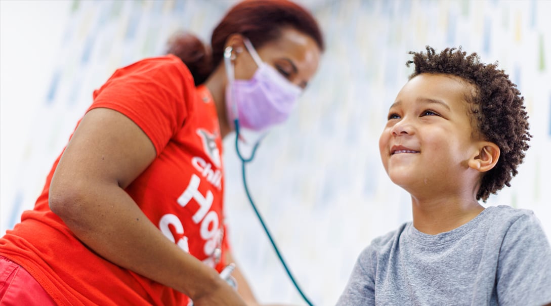 A Black female practitioner takes the blood pressure of a Black pre-school aged male patient.