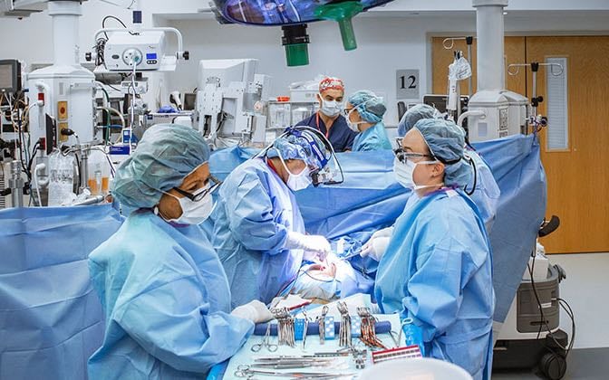 A cardiac theatre scene featuring several surgeons, nurses, and practitioners and the young patient.