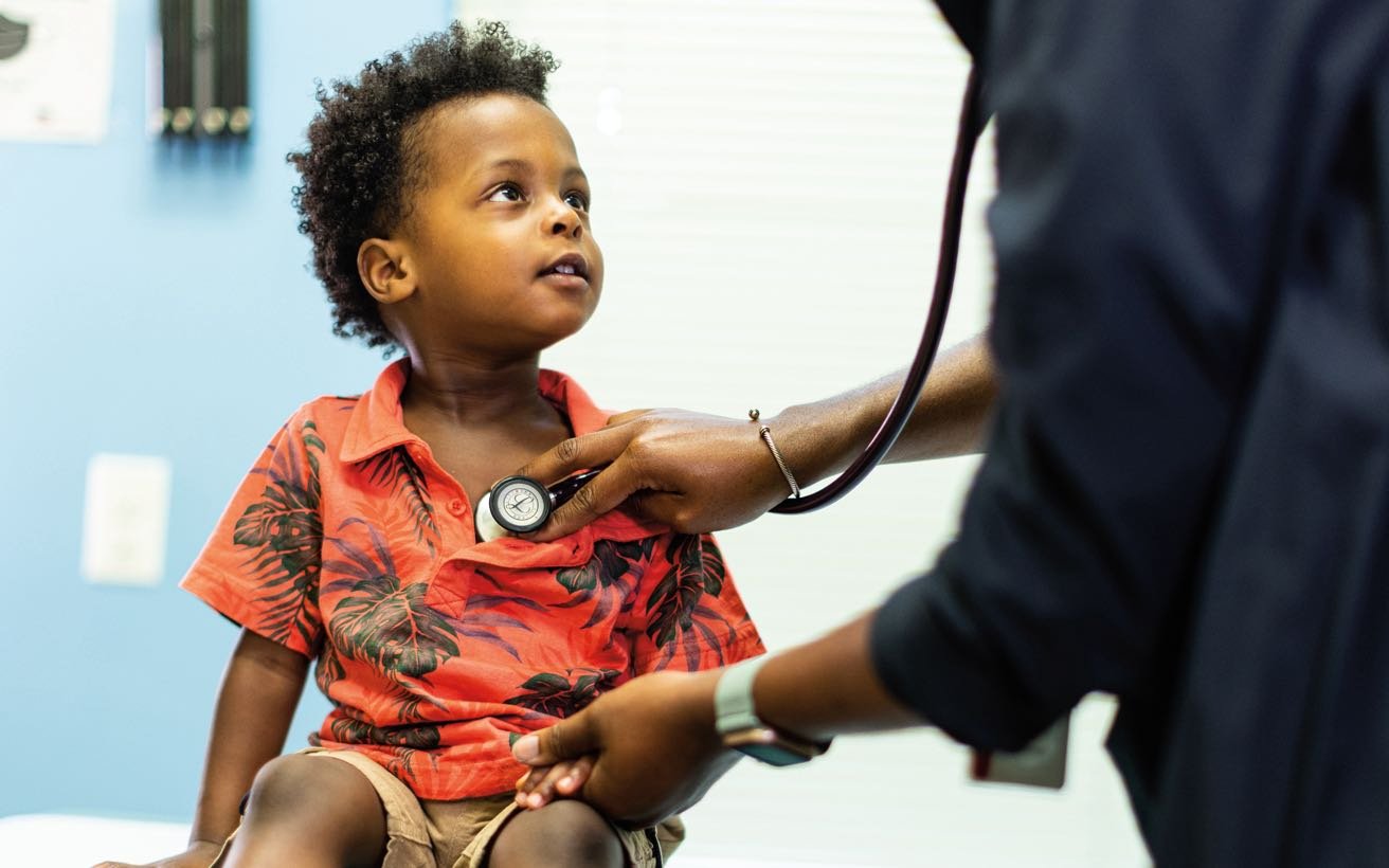 A Black pre-school aged patient gets their heart checked by a Black provider.