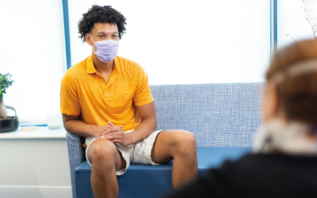 A teenaged Black male patient speaks with a behavioral health professional.