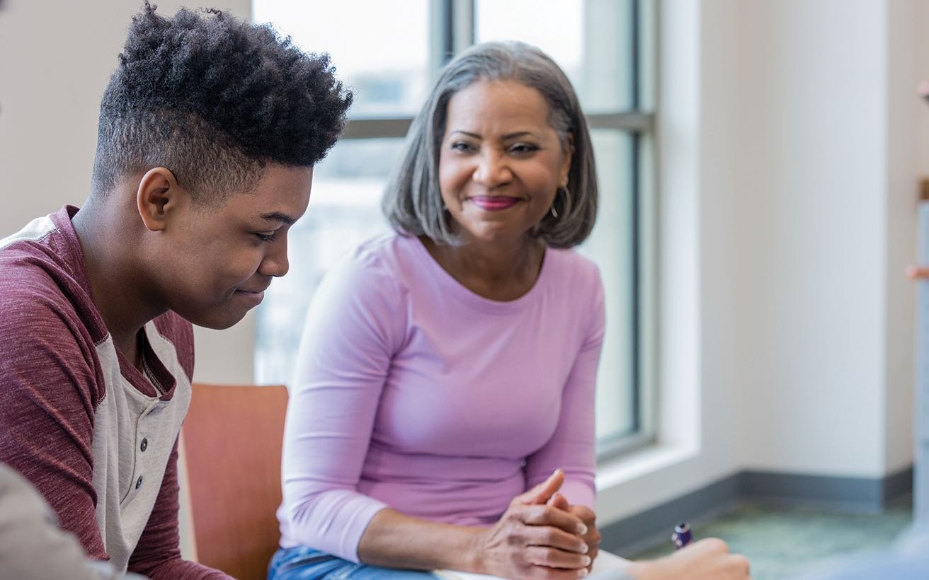 A Black male high school student sits next to a Black female adult.