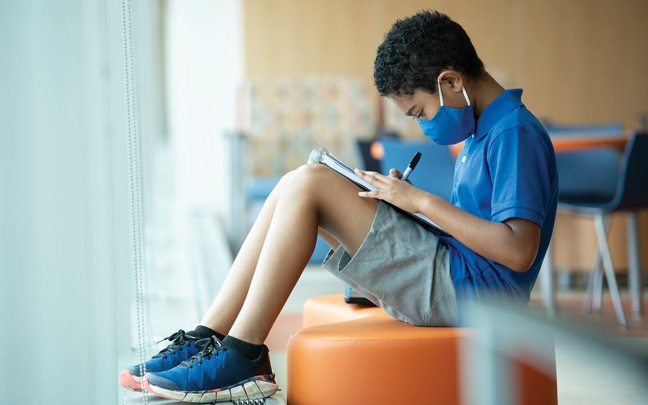 A Black elementary school-aged boy works on a drawing at a clinic.