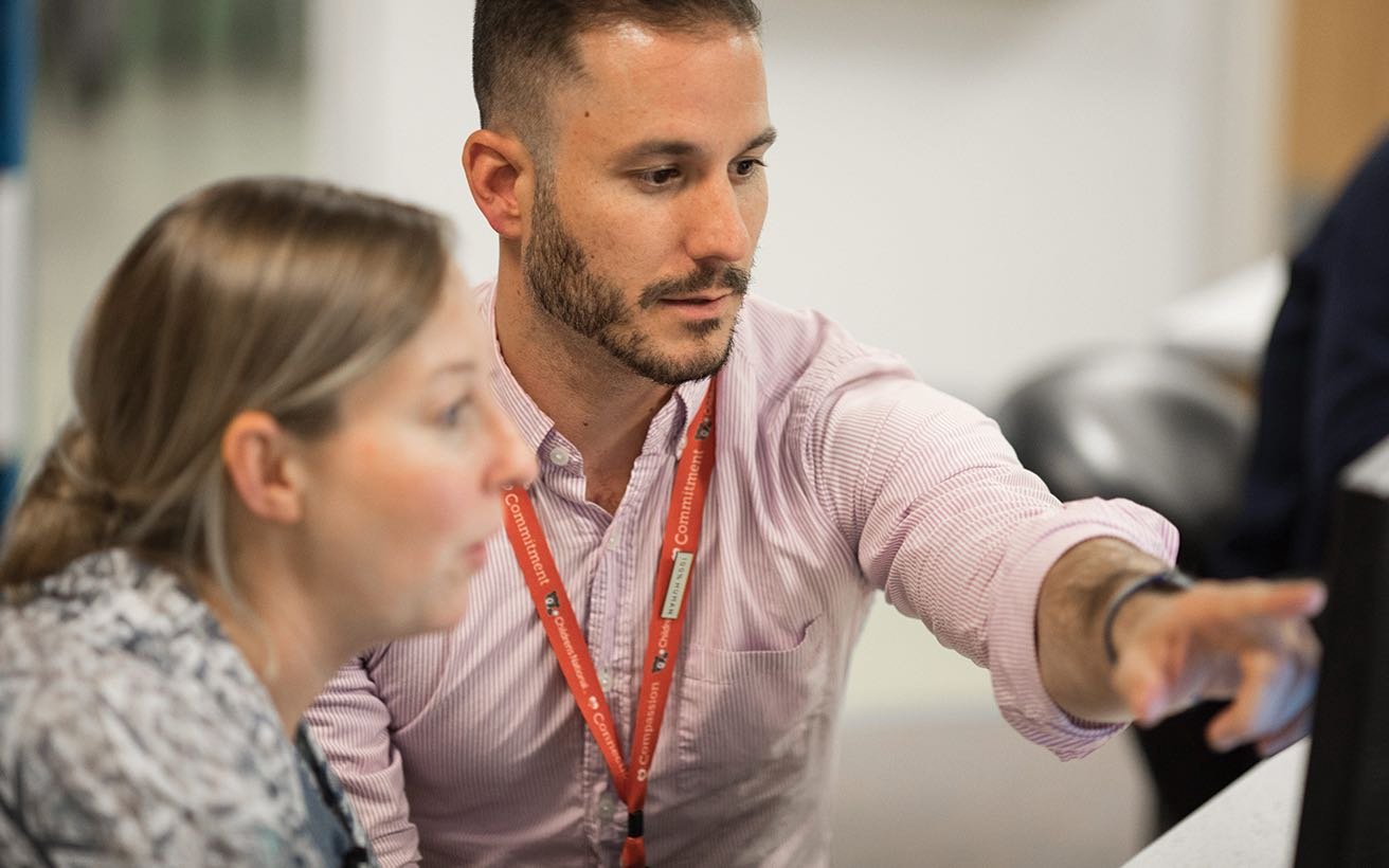 Two practitioners, one male, one female, confer at a computer screen.