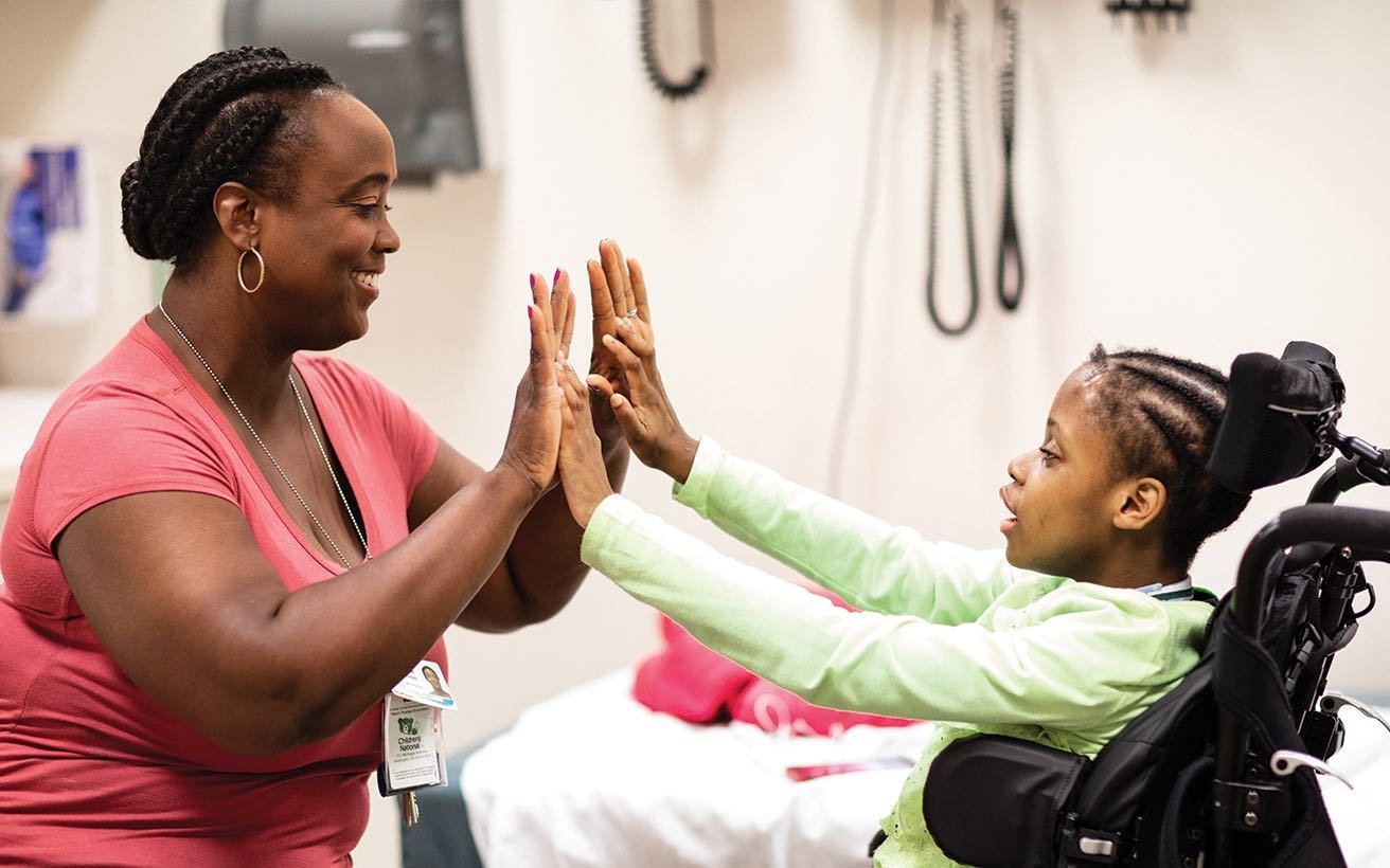 A Black, female neurology practitioner high fives with a Black elementary school-aged patient who uses a wheelchair.