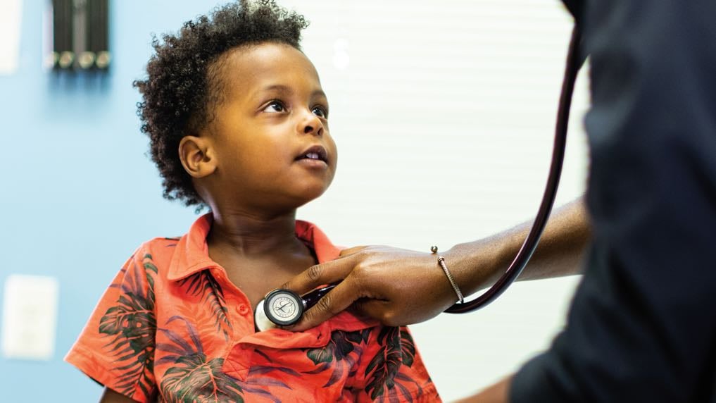 A Black pre-schooled aged boy is examined by a practitioner.