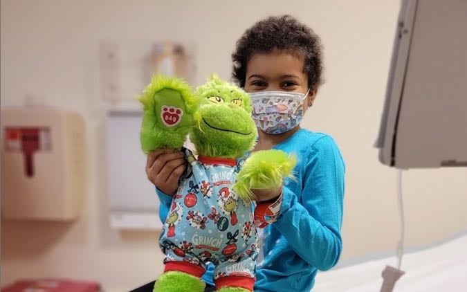 A young female patient of color poses with her Grinch doll.