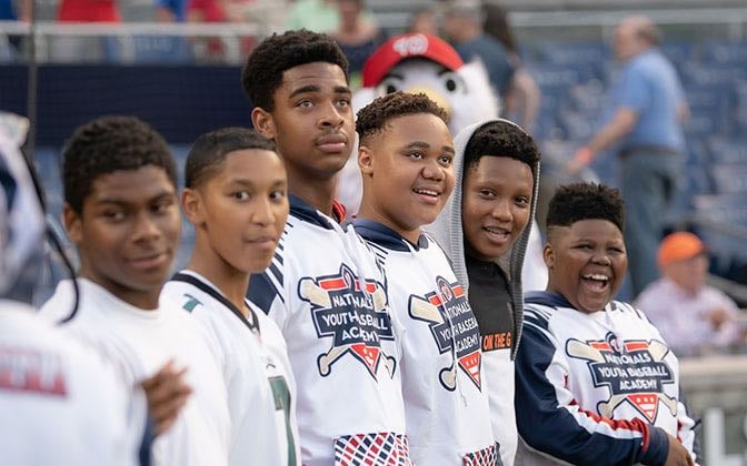 Six Black male teenaged members of the Nationals Youth Baseball Academy smile for a group photo at the stadium.