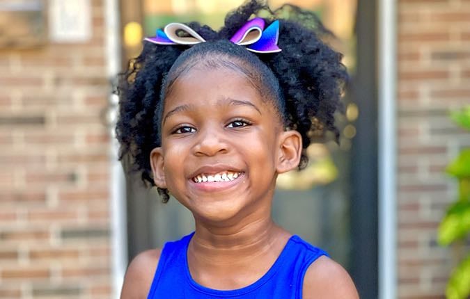 A Black elementary school-aged female patient smiles radiantly.