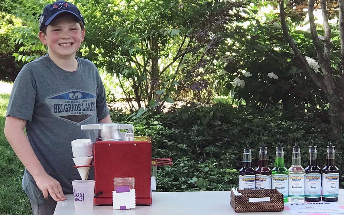 Young fundraiser standing at their shaved ice stand.