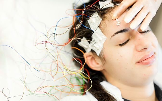 A teen patient undergoes testing; there are electrodes affixed to their head.