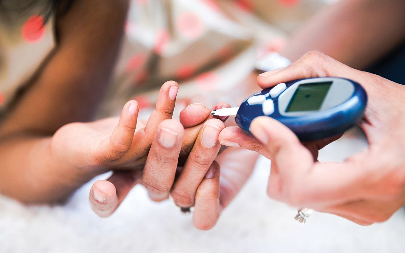 Close-up photo of a nurse taking blood from the fingertip of a young diabetes patient.