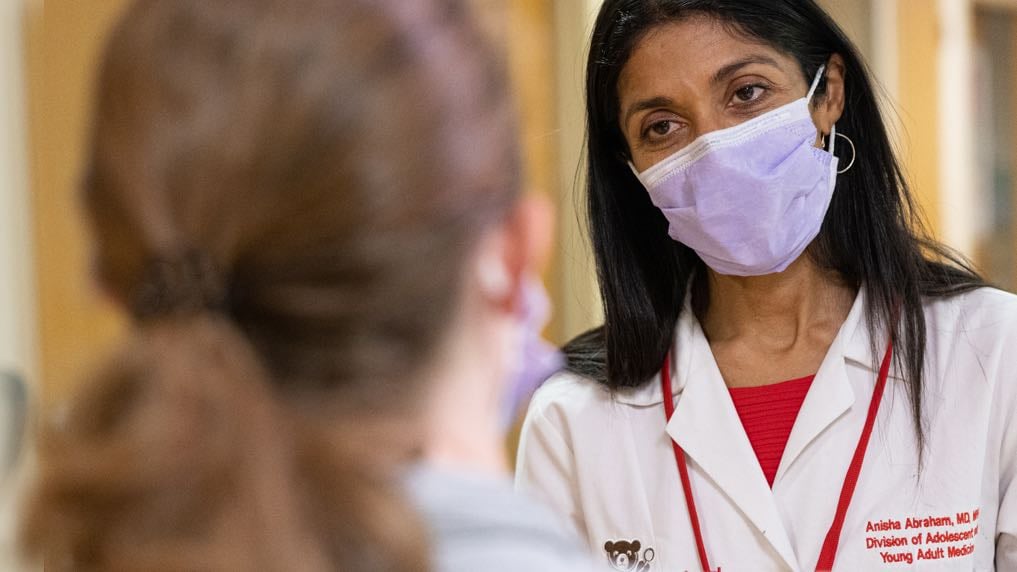 Photo of Dr. Anisha Abraham, a South Asian woman, conferring with another practitioner, whose back is to the camera.