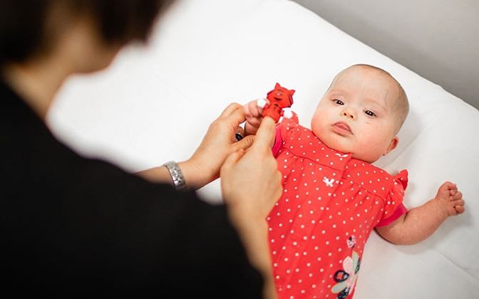 An infant patient focuses on a toy presented to them by an adult.