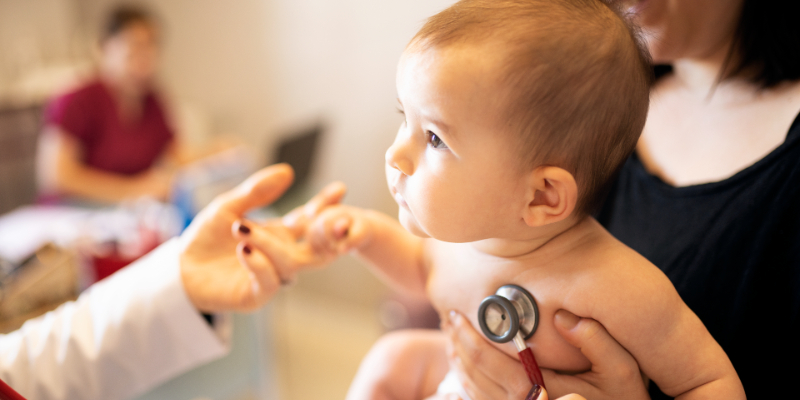 Baby being held and provider is using a stethoscope to diagnose.