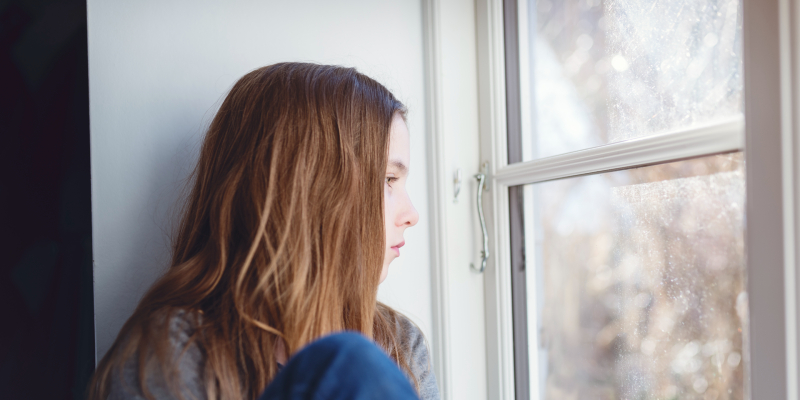 A sad teenage girl looking outside the window. 