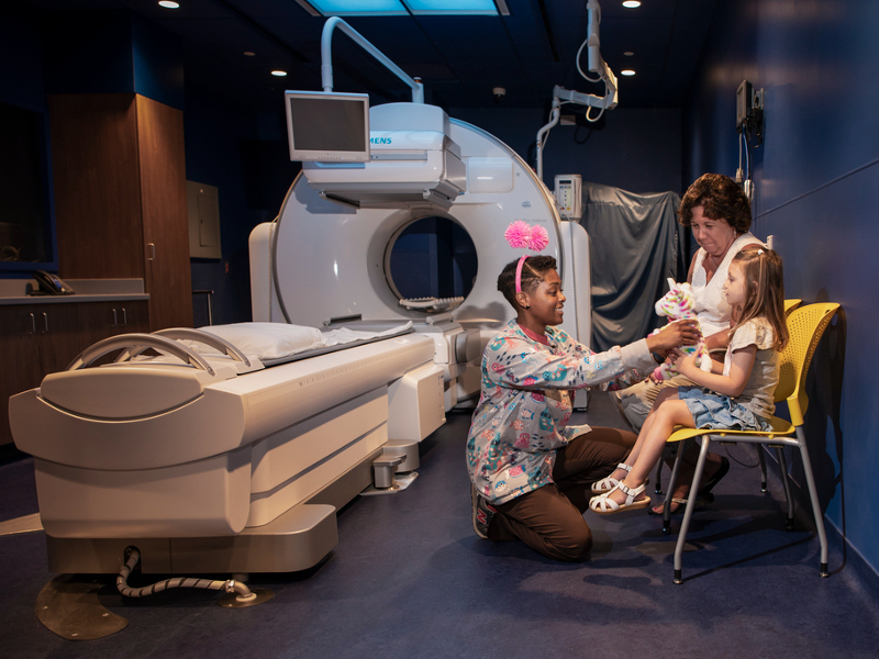 Nurse giving girl a stuffed animal in MRI imaging room