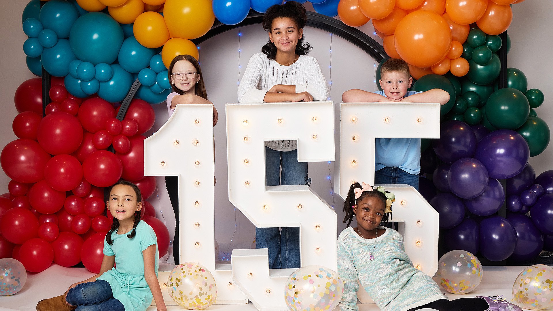 Children surrounded by balloons and standing around a 155 decorative boxes