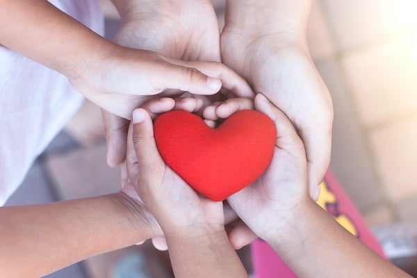 Hands of a child and parent holding a red heart shape.
