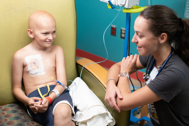 Child patient wearing an IV line talks with a squatting female care provider 