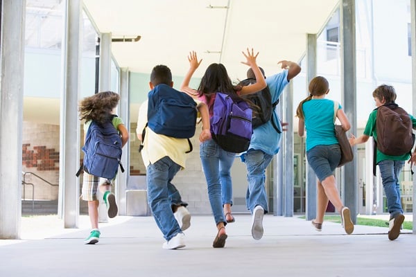 Kids wearing backpacks run down a school hallway.
