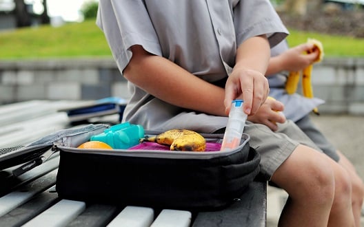 A child sits next to their lunchbag and holds an epi-pen.