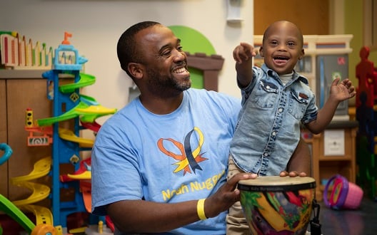 Father plays a drum with his toddler son as they both smile