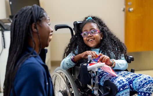 A girl in a wheelchair chats with her nurse