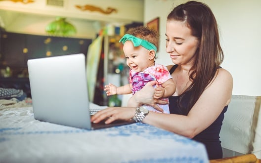 A mother sits with her infant daughter on her lap while working on her home computer.